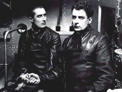 sort hvid billede fra stumfilmen Himmelskibet, to mænd i læderjakker sidder i et skib, stirrende intenst